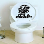 Toilet with humorous It's a Crap decal, featuring a parody graphic on the seat lid.