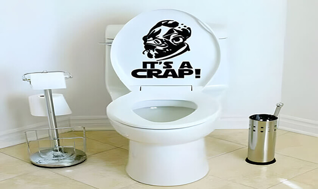 Toilet with humorous It's a Crap decal, featuring a parody graphic on the seat lid.